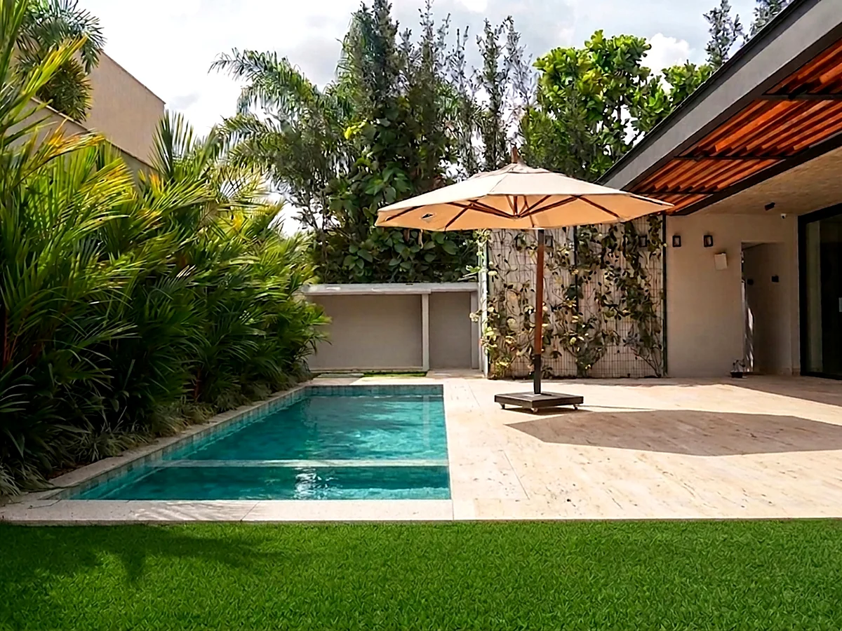 Piscina e área de lazer de casa residencial entregue pela HC Engenharia, com deck em travertino e cobertura ripada em madeira